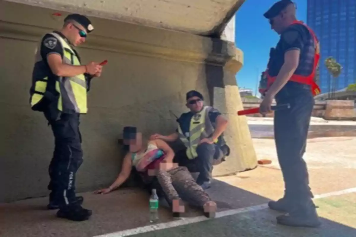 Tres policías asisten a una persona sentada en el suelo bajo un puente.