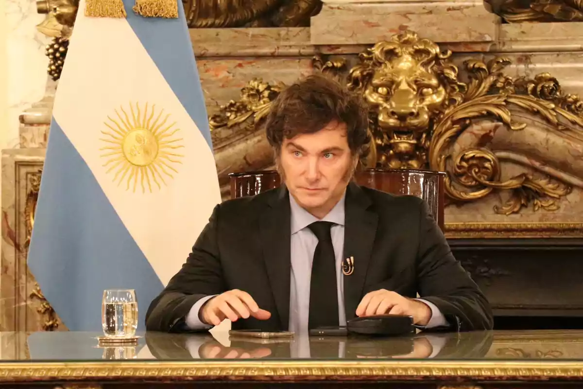 Hombre sentado en una mesa con una bandera de Argentina detrás.