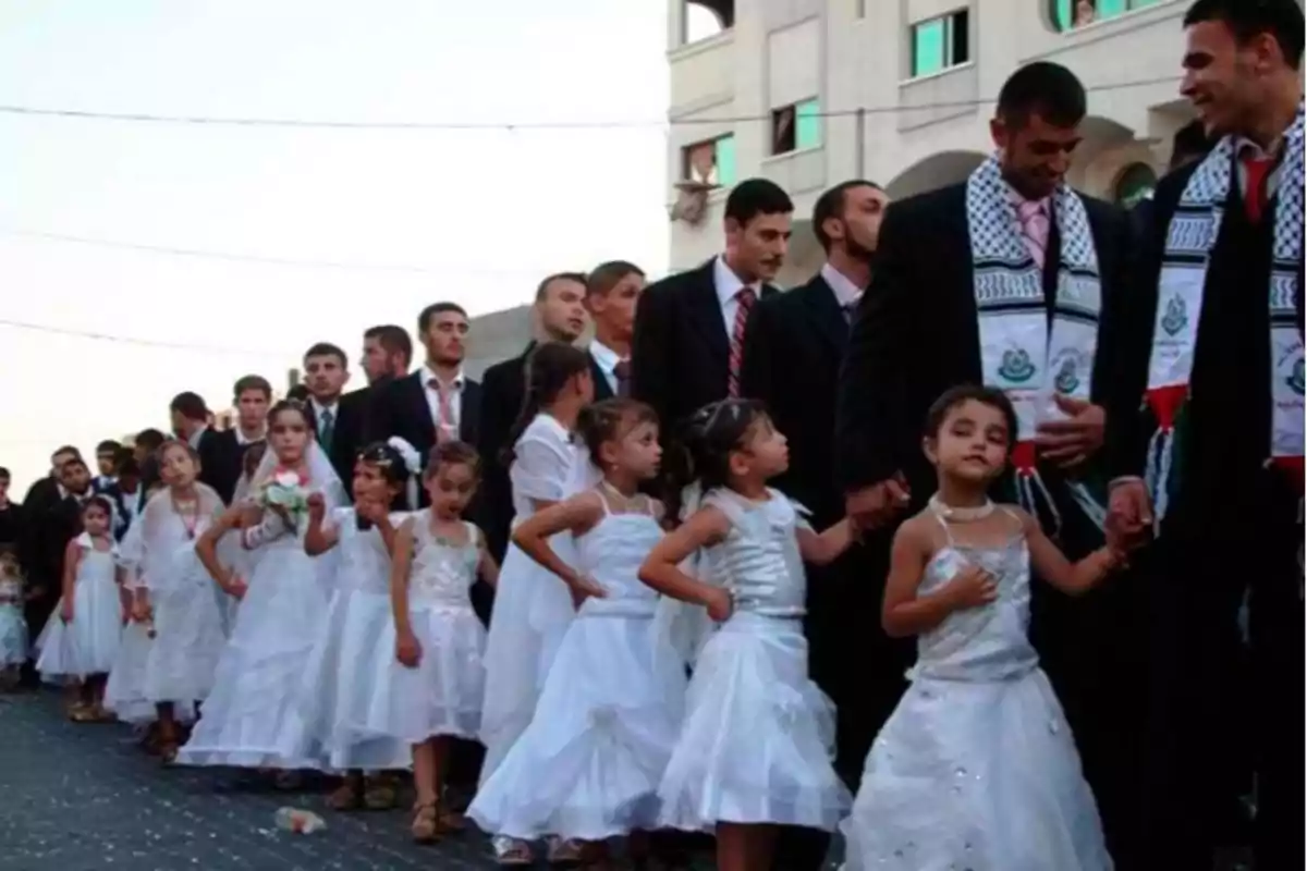 Un grupo de hombres y niñas vestidas de blanco caminan en fila en un evento al aire libre.