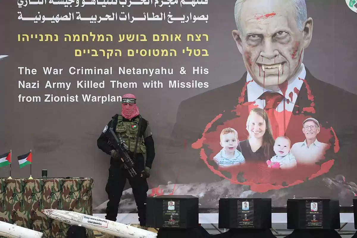 Un hombre enmascarado y armado está de pie frente a un cartel que muestra una imagen editada de una figura política con sangre y rostros de personas, junto a misiles y banderas palestinas.