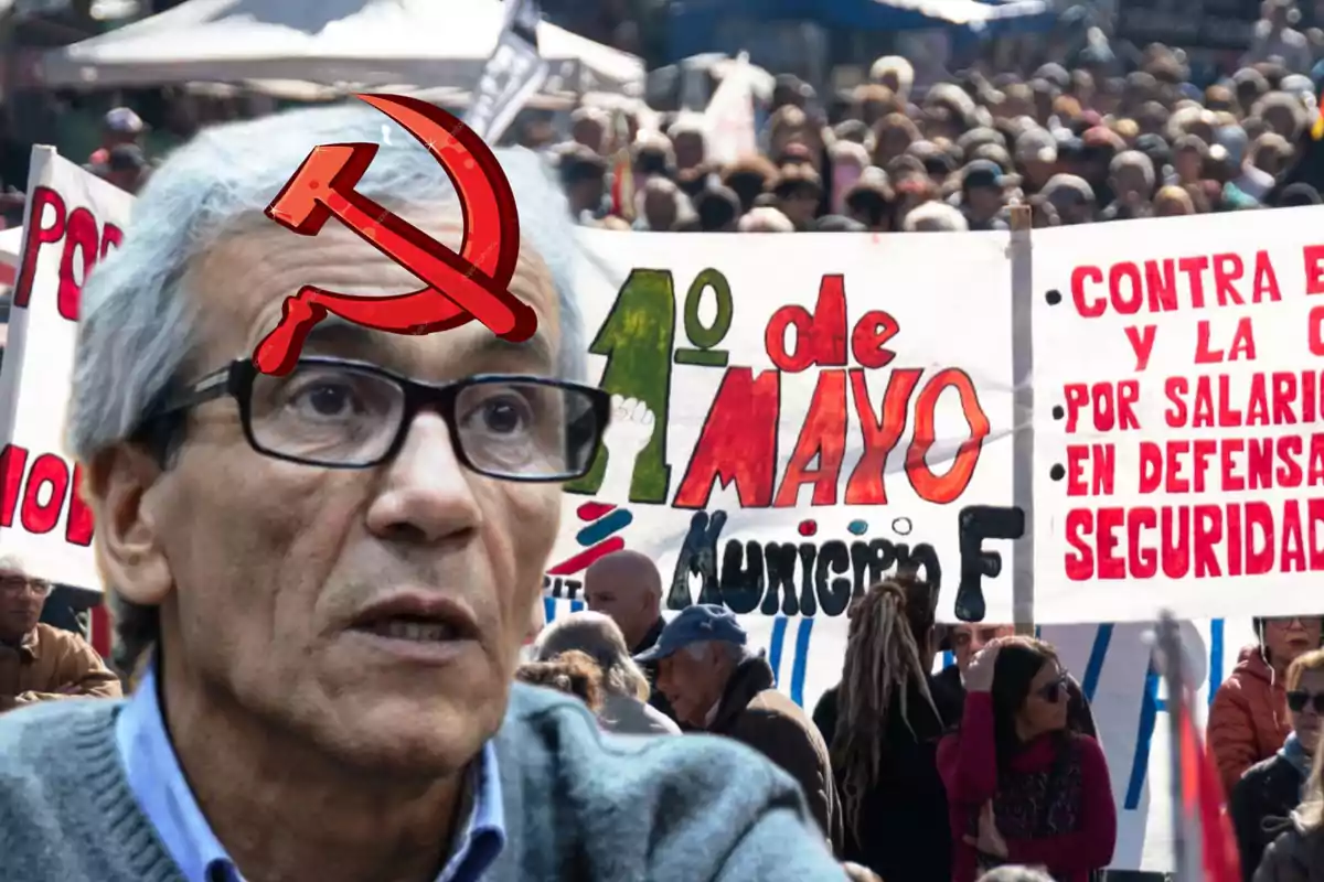 Un hombre con gafas y un símbolo comunista en la frente aparece en primer plano mientras al fondo se observa una multitud con pancartas del 1 de mayo.