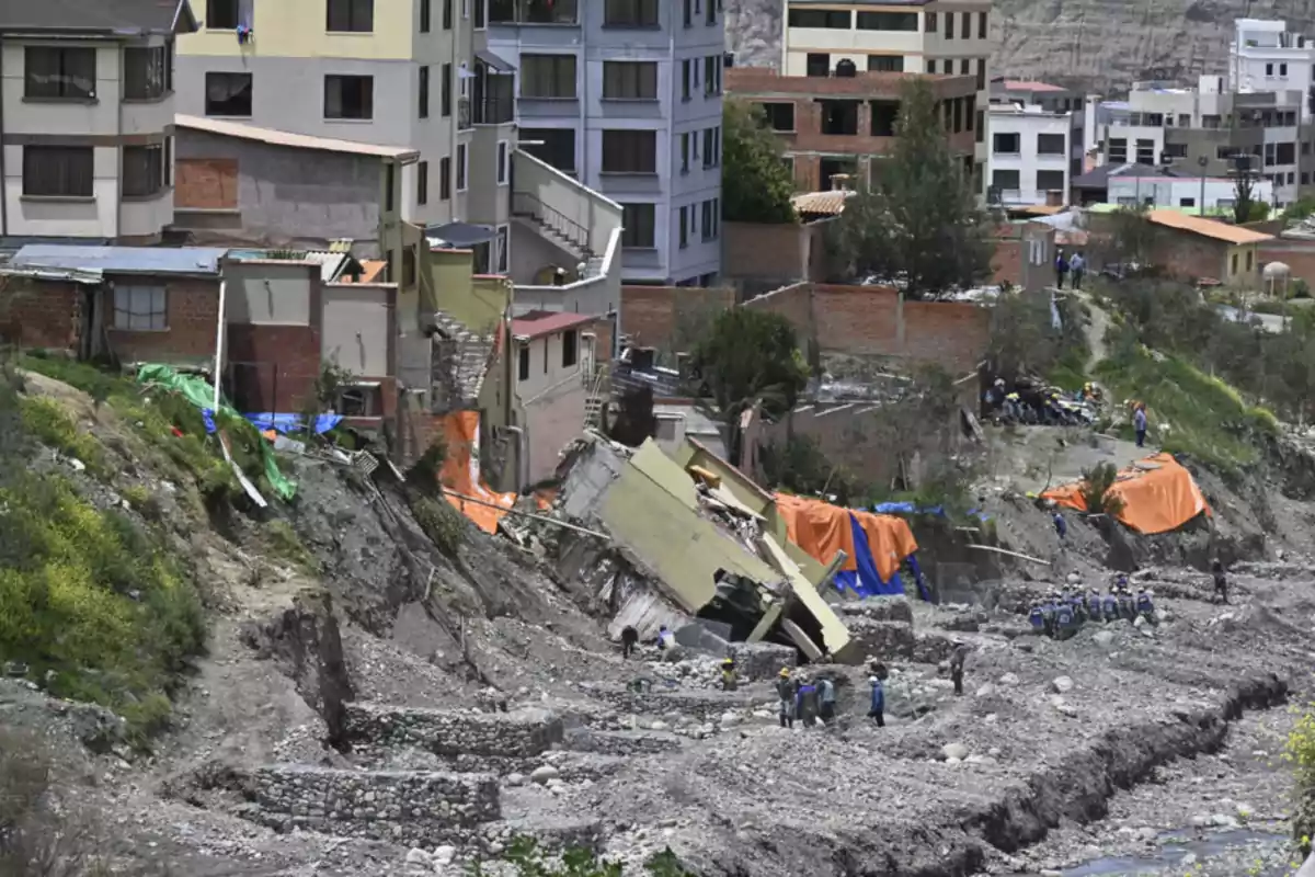 Buildings on a hillside with a landslide and collapsed structures, while people observe and work in the affected area.