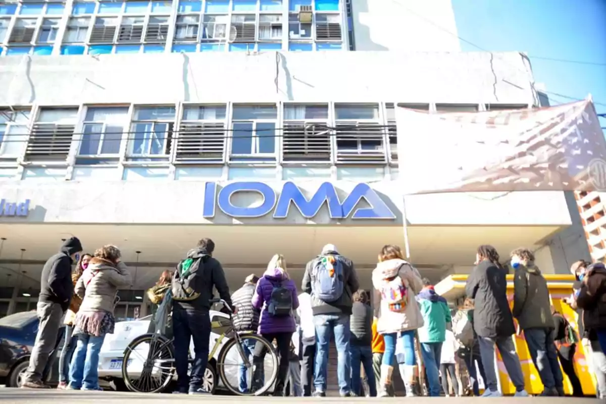 Personas reunidas frente a un edificio con el letrero de IOMA.