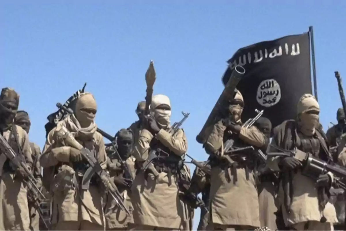 Grupo de personas armadas con vestimenta militar y una bandera negra.