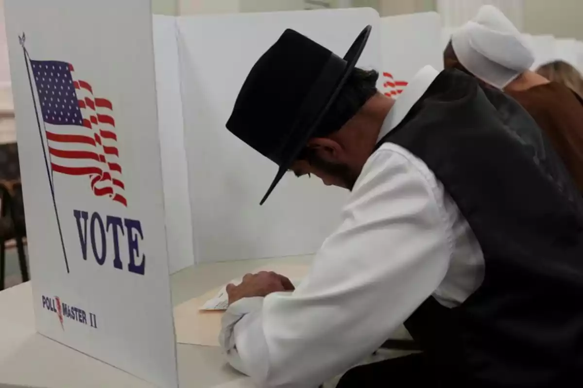 Persona con sombrero votando en una cabina electoral con bandera de Estados Unidos.