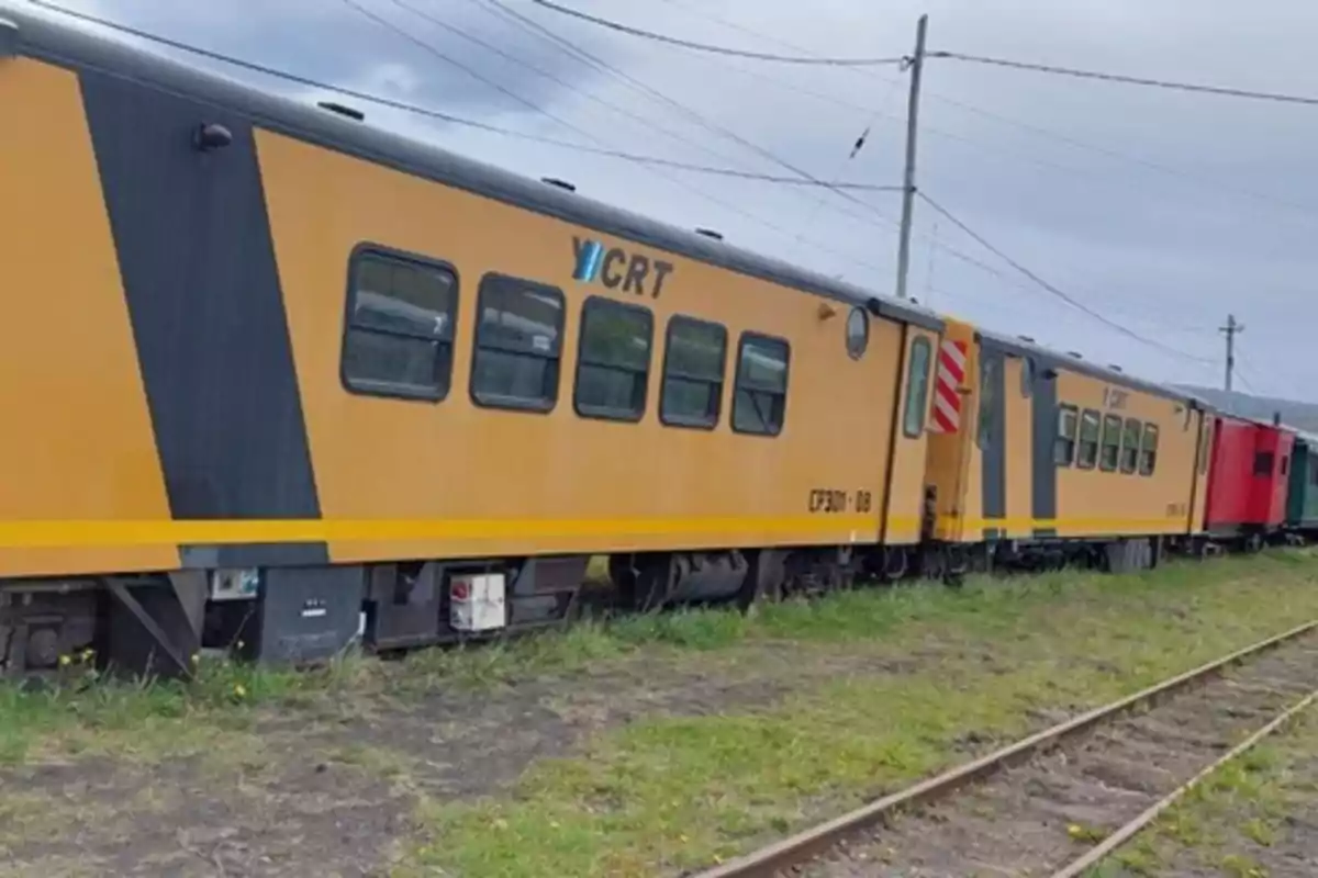 Un tren amarillo y negro estacionado sobre vías en un entorno rural.