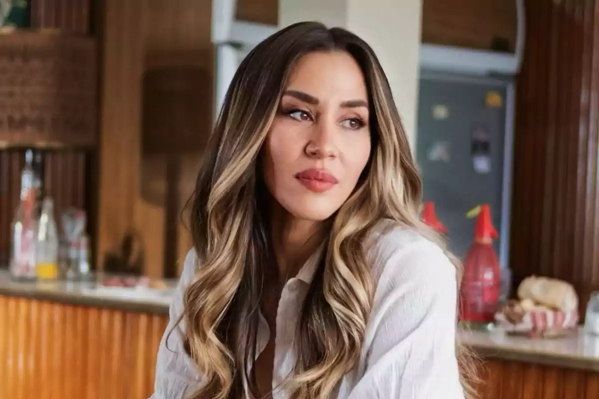 Mujer con cabello largo y ondulado en un ambiente interior con fondo de cocina.