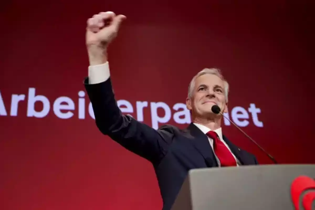 Un hombre en un podio con fondo rojo y texto "Arbeiderpartiet" levanta el puño en señal de triunfo.