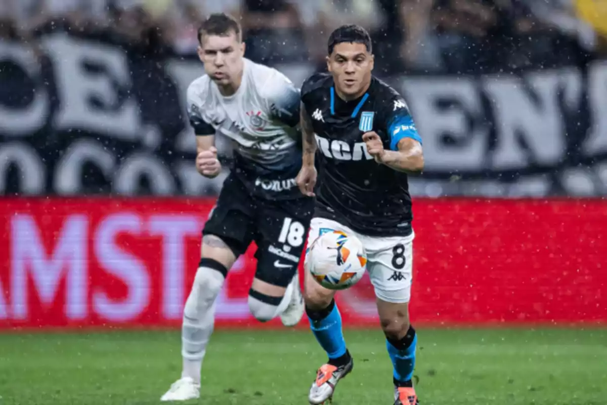 Dos jugadores de fútbol compiten por el balón en un partido bajo la lluvia.