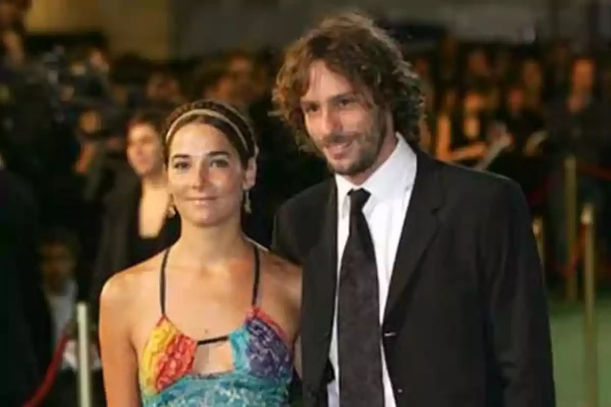 Una pareja posando en un evento formal con fondo de personas y luces.