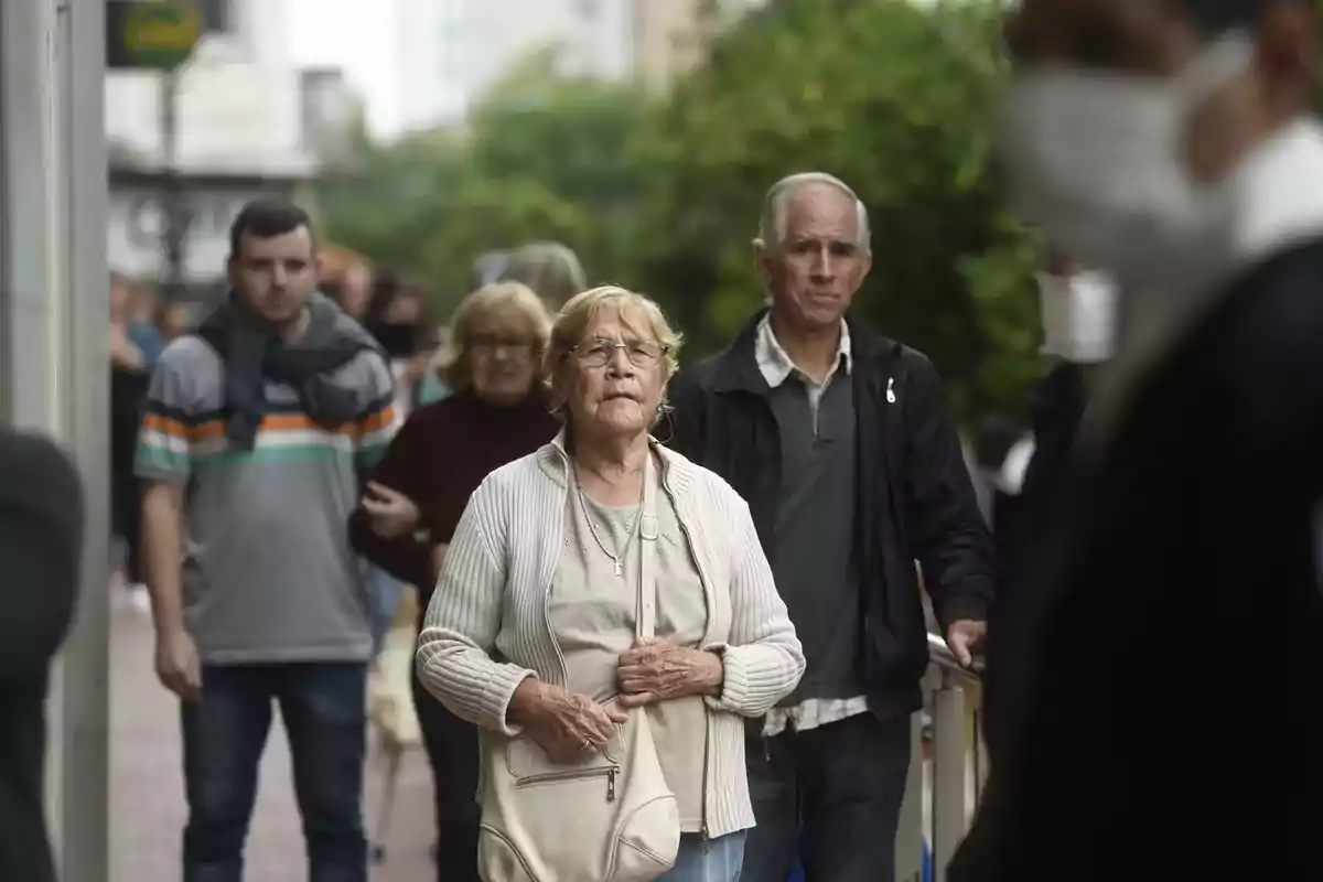 Un grupo de personas camina por una acera en un entorno urbano, algunas de ellas llevan mascarillas.