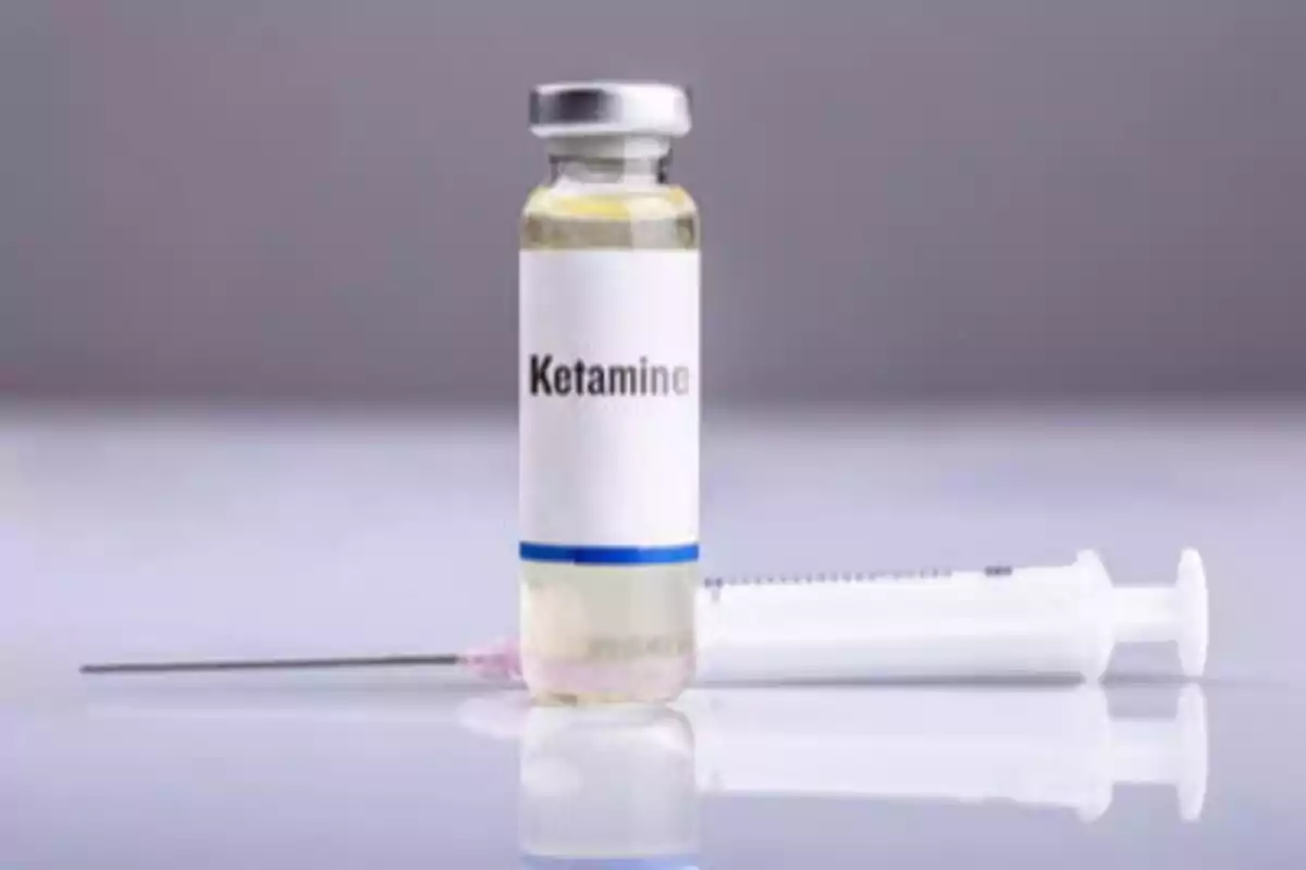 Un vial de ketamina junto a una jeringa sobre una superficie reflectante.