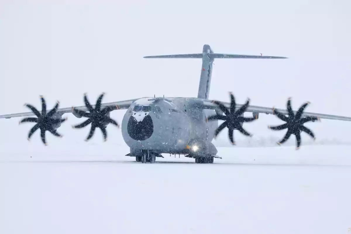 A military transport plane on a snow-covered runway with spinning propellers.