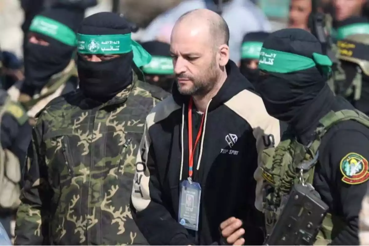 Un hombre escoltado por personas con uniformes militares y pasamontañas negros con cintas verdes en la cabeza.