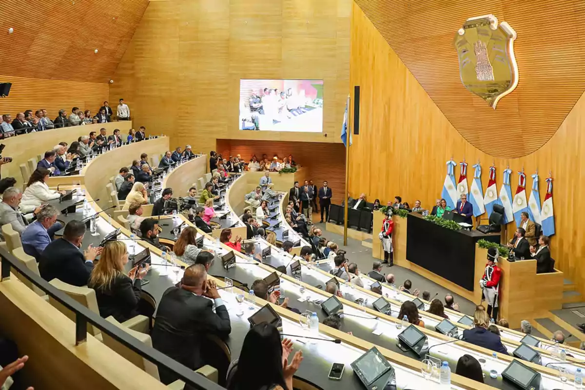 Una asamblea legislativa en sesión con personas sentadas en un auditorio semicircular y banderas en el estrado.