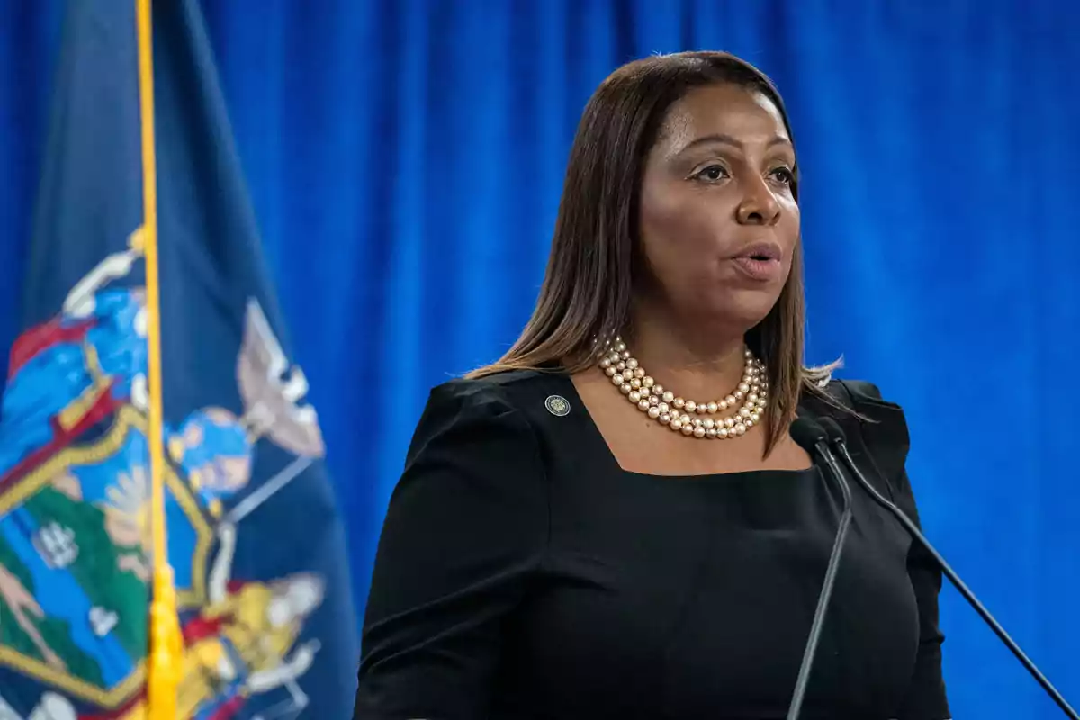 A woman speaking at a podium with a blue background and a flag beside her.