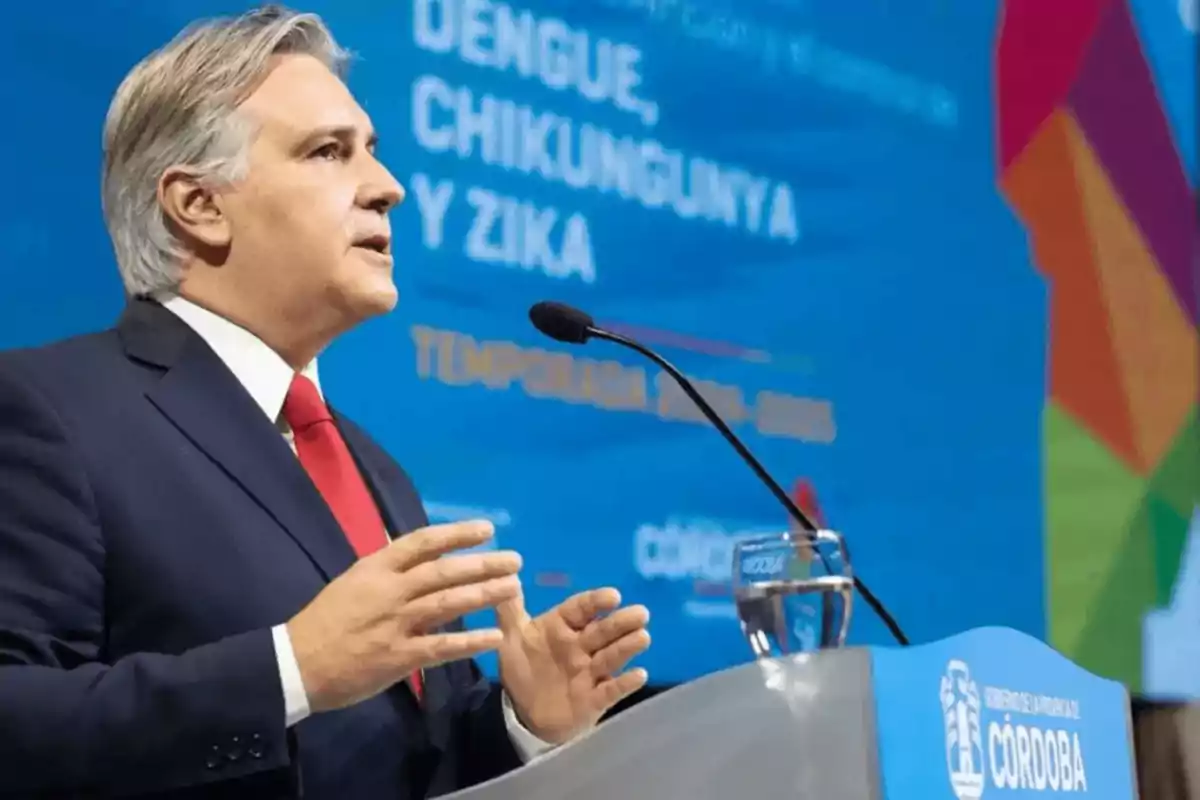 Un hombre de traje y corbata roja hablando en un podio con un micrófono, con un fondo azul que menciona "Dengue, Chikungunya y Zika" y el logo del Gobierno de la Provincia de Córdoba.