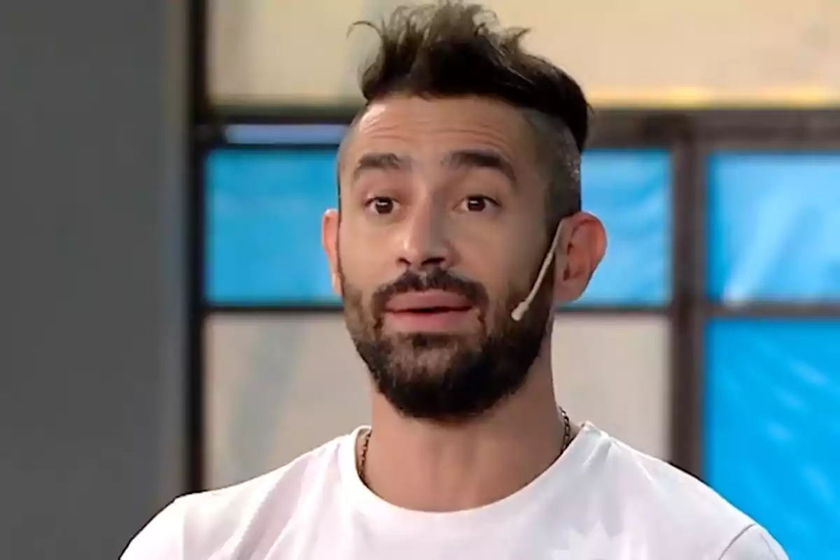 A man with a beard and a microphone in a television studio.