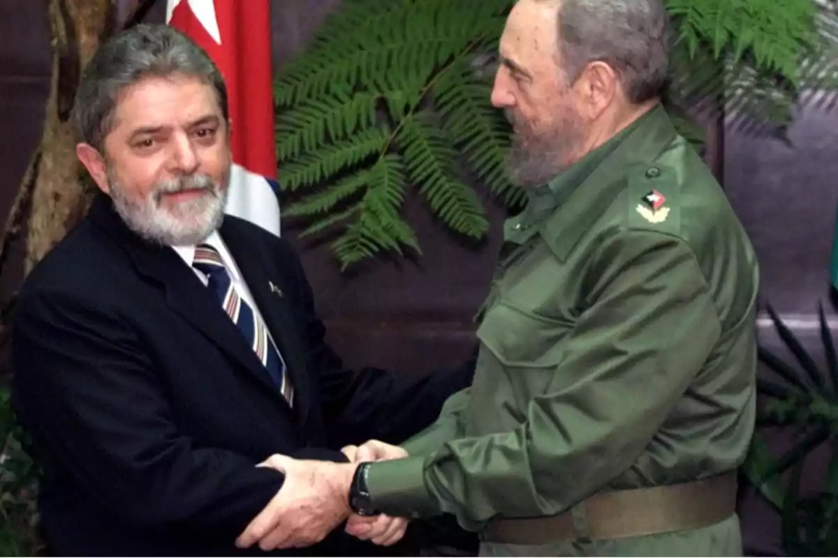 Dos hombres se dan la mano en un entorno con plantas y una bandera de fondo.