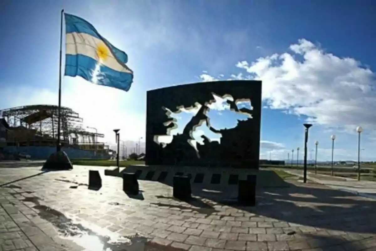 Monumento con la silueta de las Islas Malvinas y una bandera argentina ondeando al viento en un día soleado.