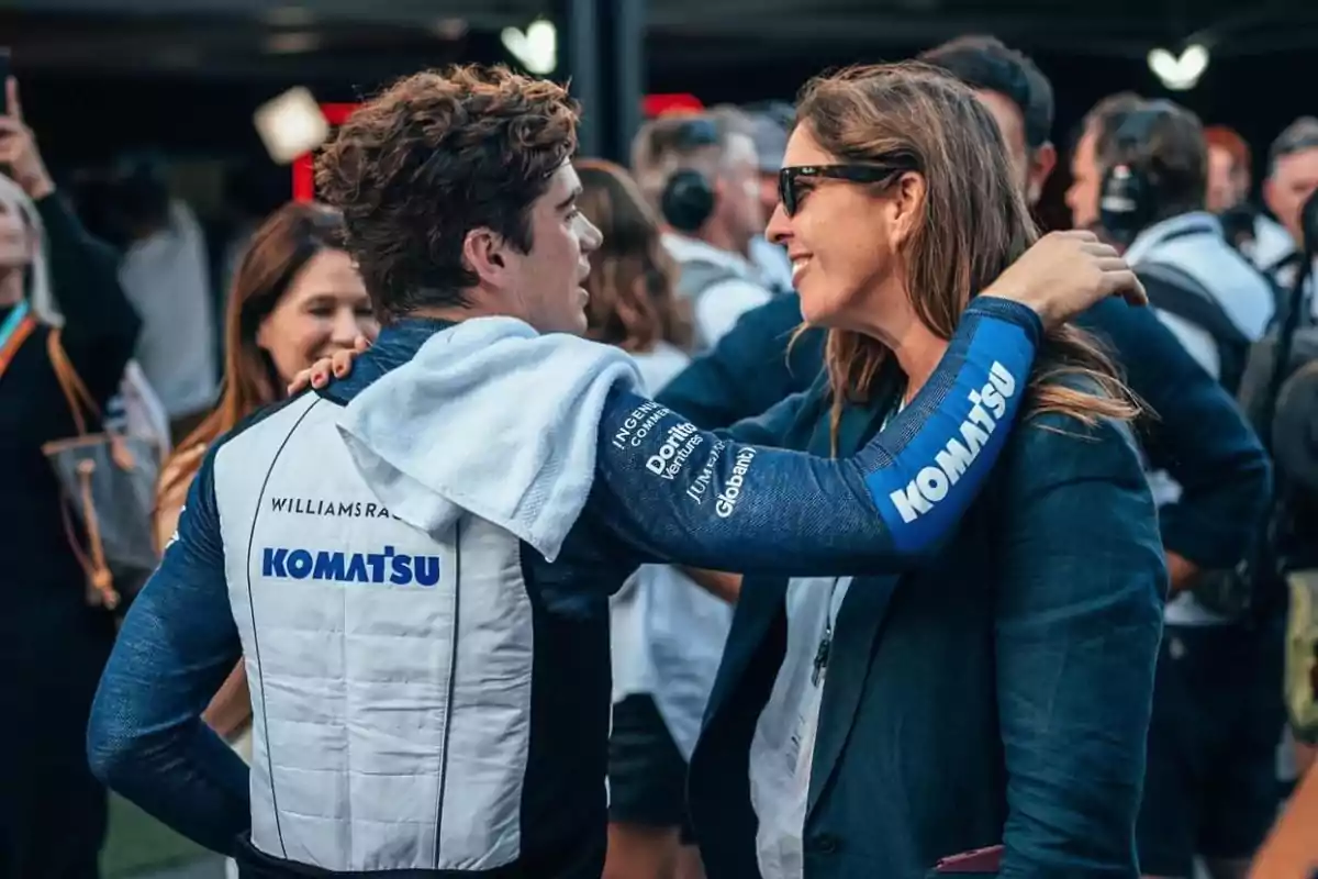 Un piloto de carreras con uniforme de Komatsu conversa y sonríe con una mujer en un evento lleno de gente.