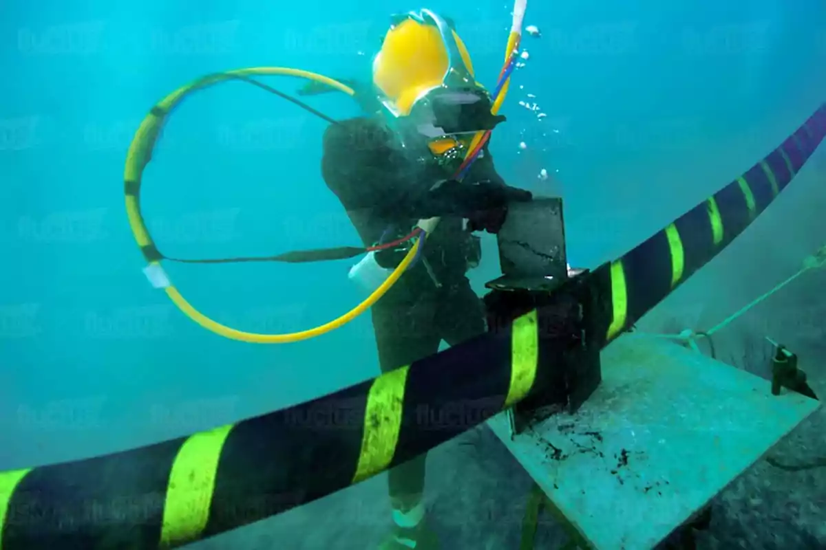 Un buzo con equipo especializado trabaja bajo el agua manipulando cables y herramientas.