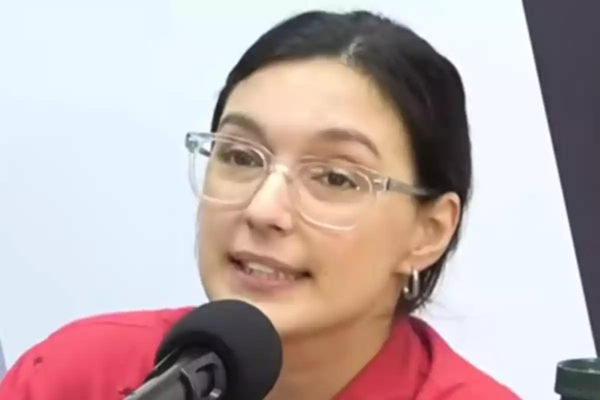 Una persona con gafas y cabello oscuro hablando frente a un micrófono.