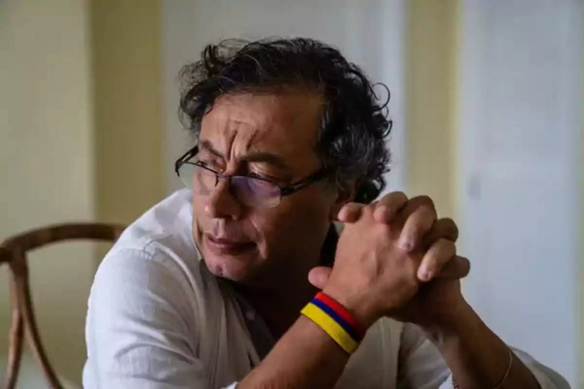 Hombre con gafas y pulsera de colores sentado con las manos entrelazadas.