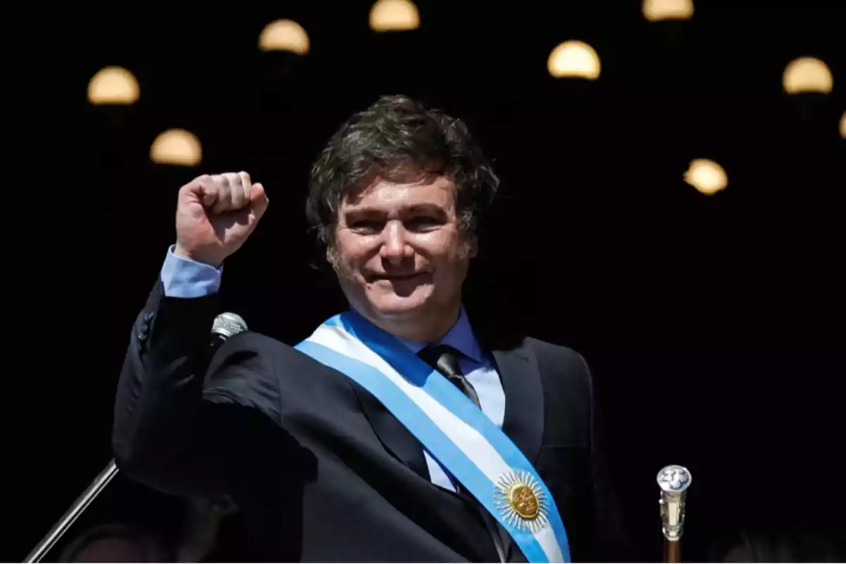 Un hombre con traje oscuro y banda presidencial levanta el puño en señal de celebración.