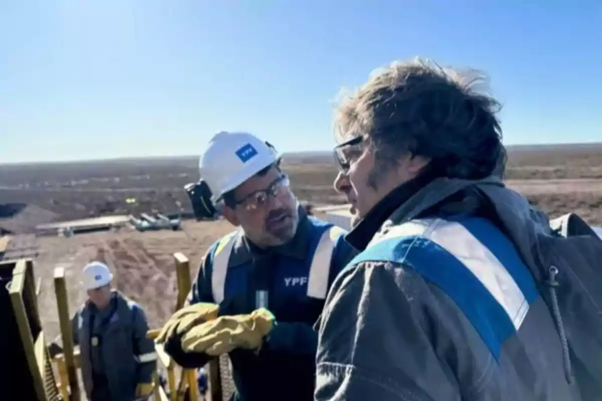 Personas con cascos y equipo de seguridad conversan en un sitio de construcción al aire libre.