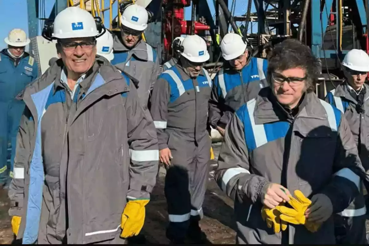 Un grupo de personas con cascos y ropa de trabajo industrial camina en un entorno de maquinaria pesada.