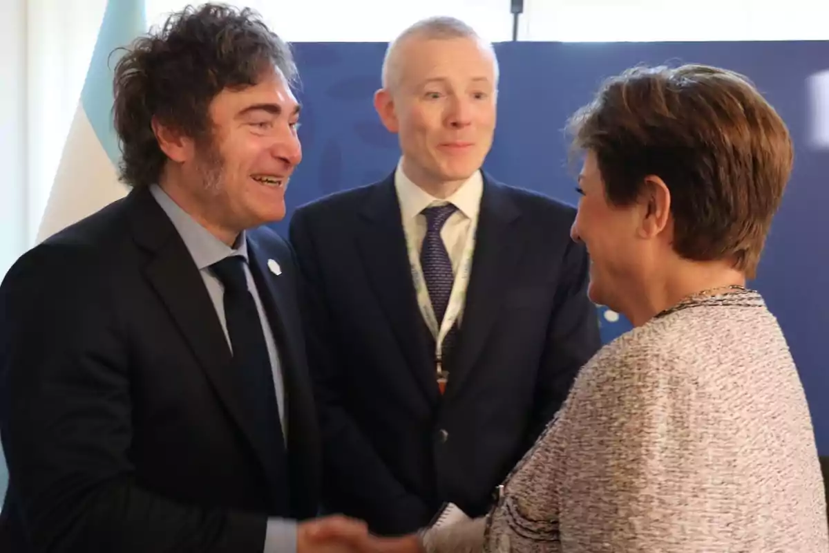 Tres personas vestidas formalmente se saludan y conversan en un evento.