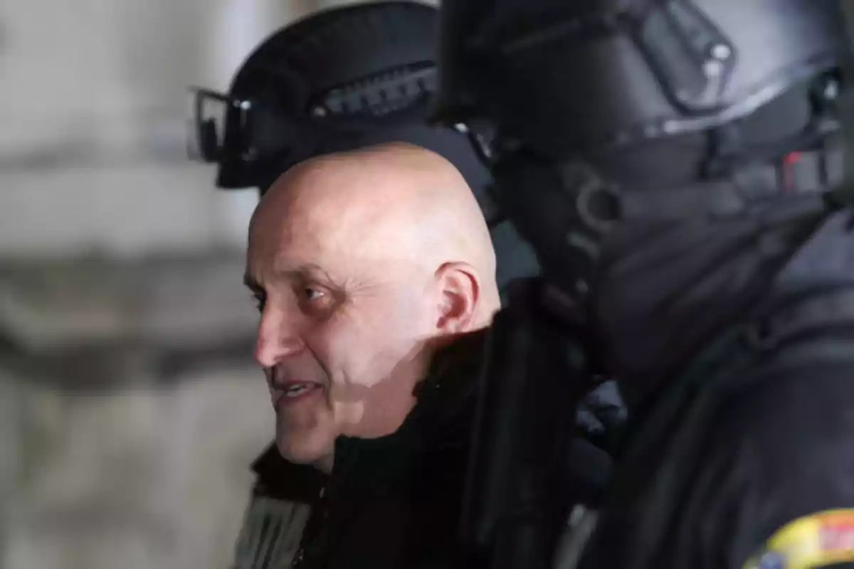 Un hombre calvo sonriendo junto a dos personas con equipo táctico.