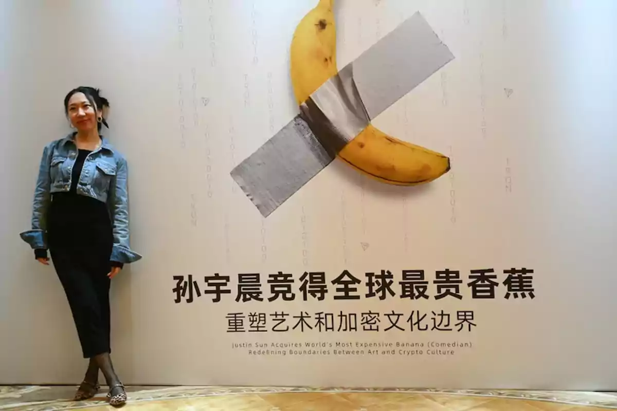 Mujer posando junto a una pared con una banana pegada con cinta adhesiva y texto en chino y en inglés.