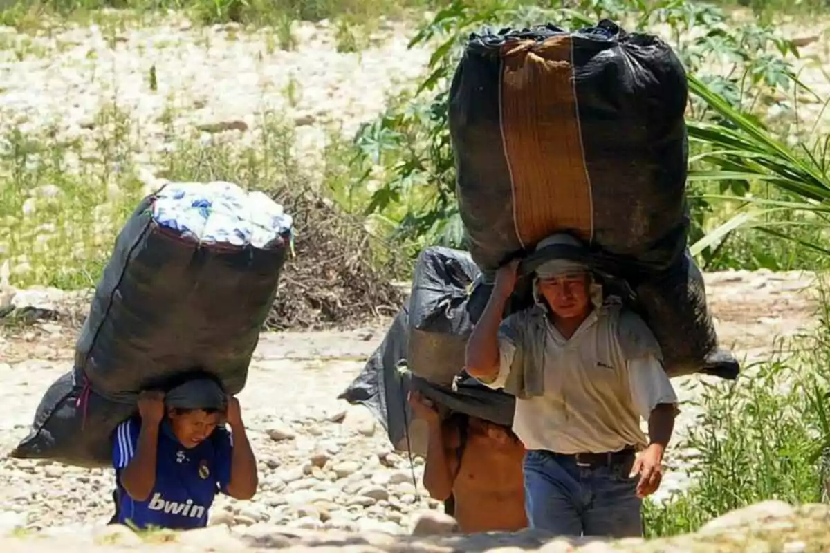 Tres personas caminan por un terreno rocoso llevando grandes bultos sobre sus espaldas.