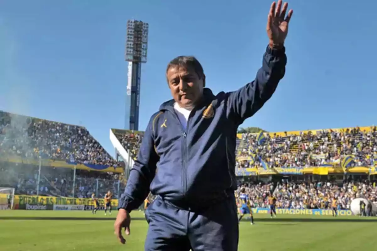 Un hombre con ropa deportiva azul saluda en un estadio lleno de espectadores.