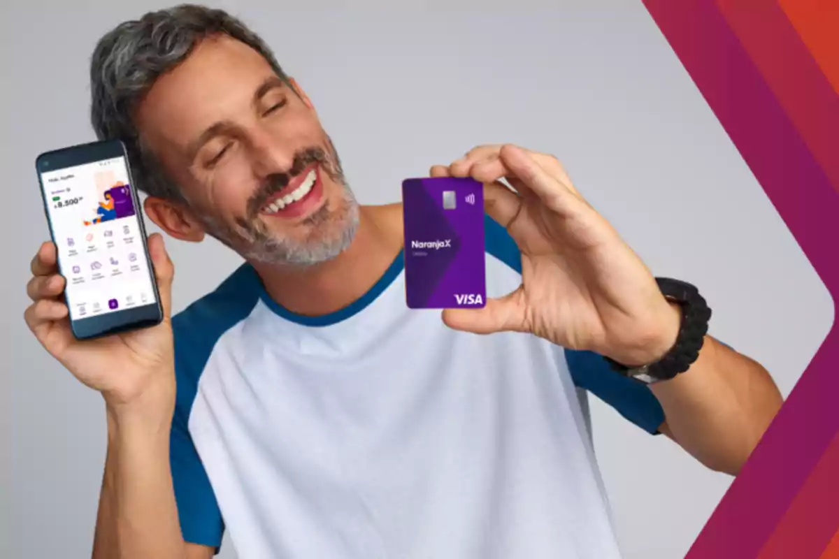 Hombre sonriente sosteniendo un teléfono móvil y una tarjeta de crédito púrpura.