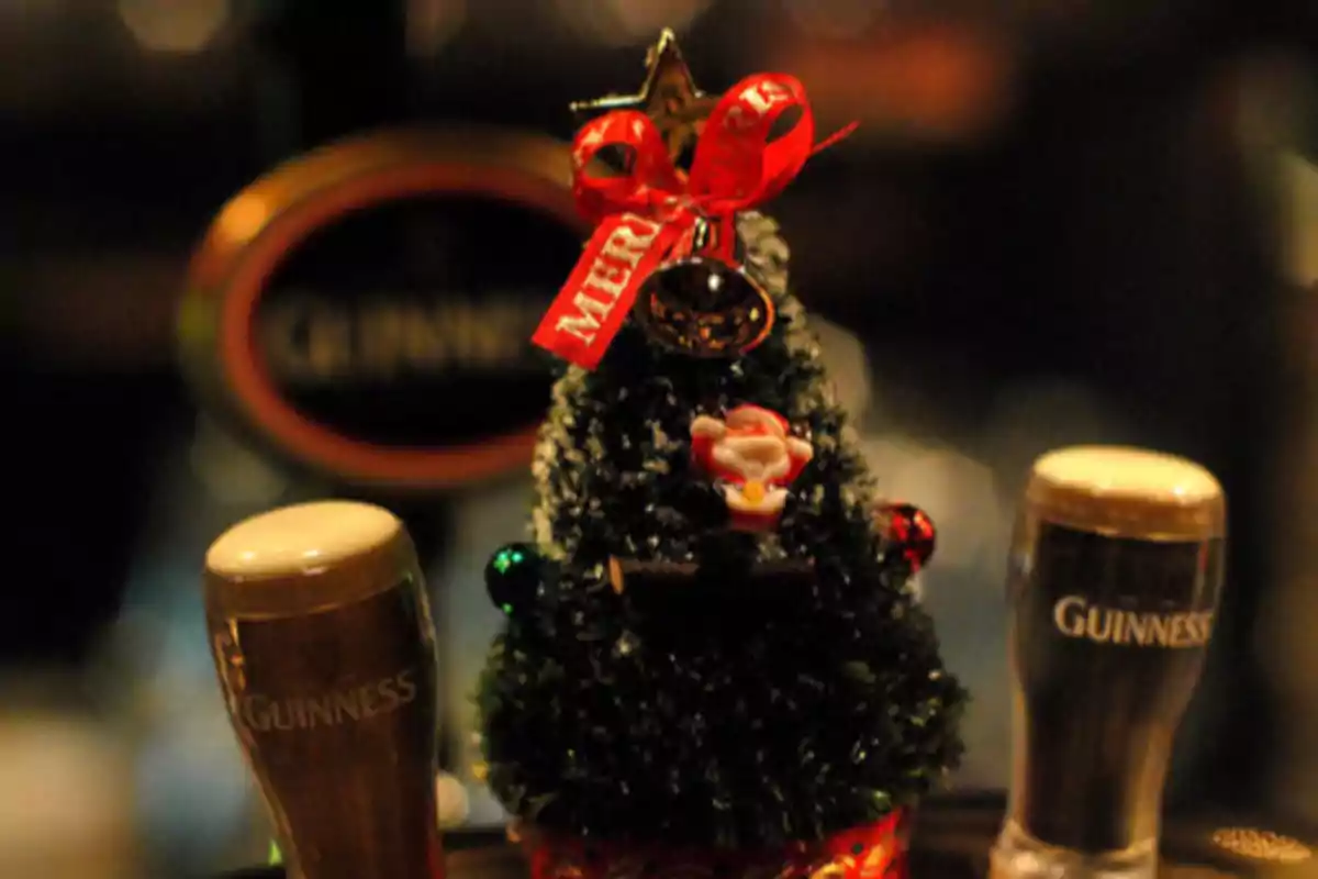 Un pequeño árbol de Navidad decorado con una cinta roja y una estrella dorada entre dos vasos de cerveza Guinness. tradición navideña en Irlanda.