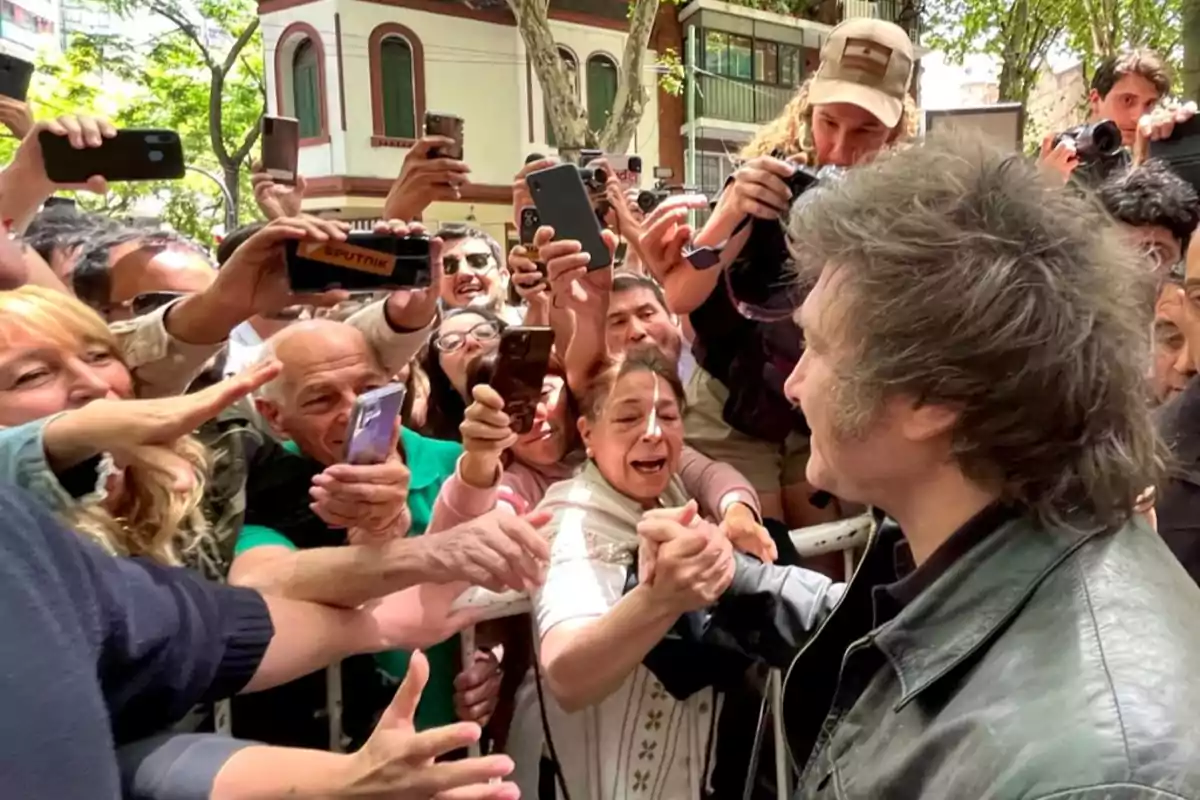 Una multitud de personas rodea a un hombre mientras le toman fotos y le estrechan la mano en una calle arbolada.