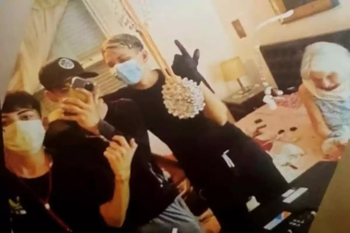 Un grupo de personas con mascarillas y guantes se toma una selfie en una habitación desordenada donde hay una persona mayor sentada en la cama.