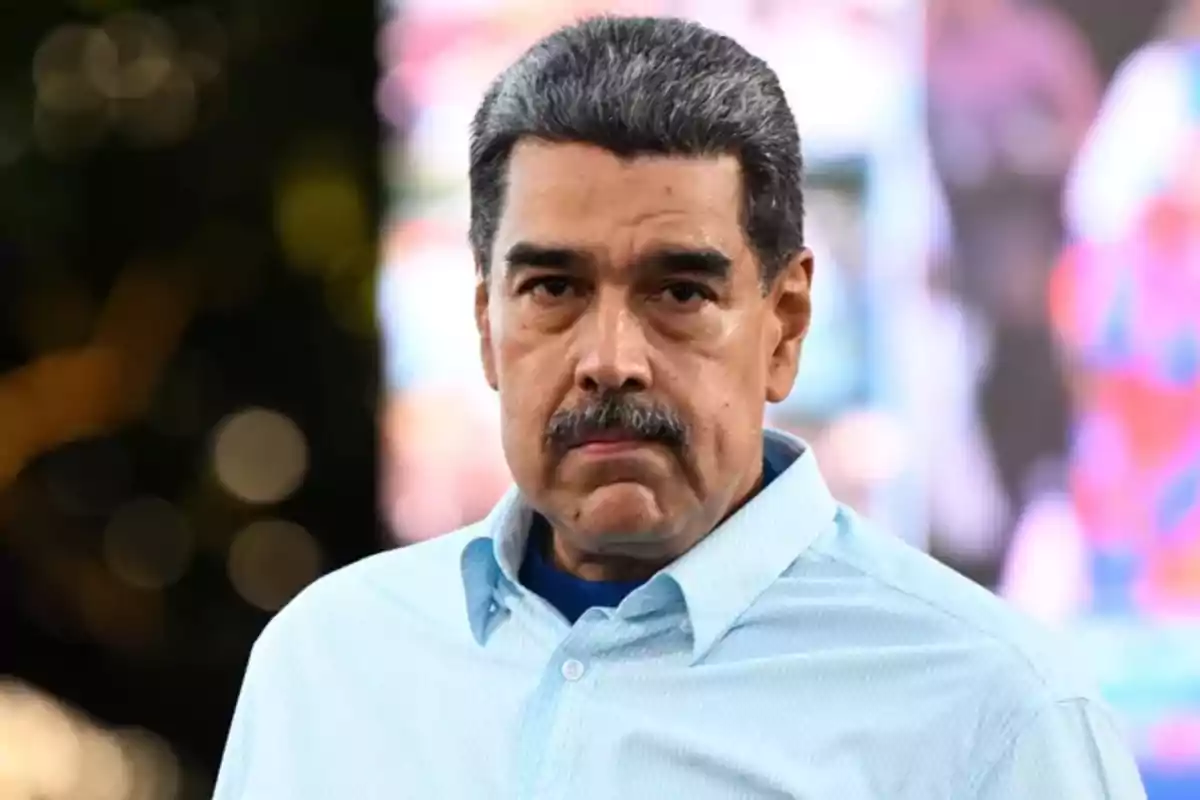 Un hombre con bigote y cabello canoso viste una camisa azul claro y está al aire libre con un fondo desenfocado.