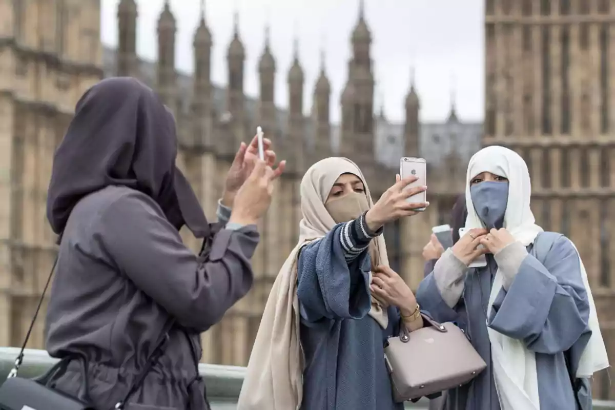 Tres mujeres con hiyab se toman selfies frente a un edificio histórico.