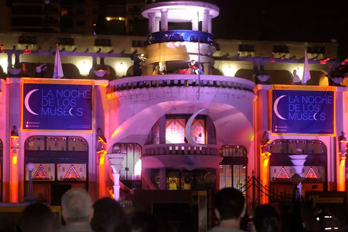 Fachada de un edificio iluminado con luces de colores durante un evento nocturno llamado "La Noche de los Museos".