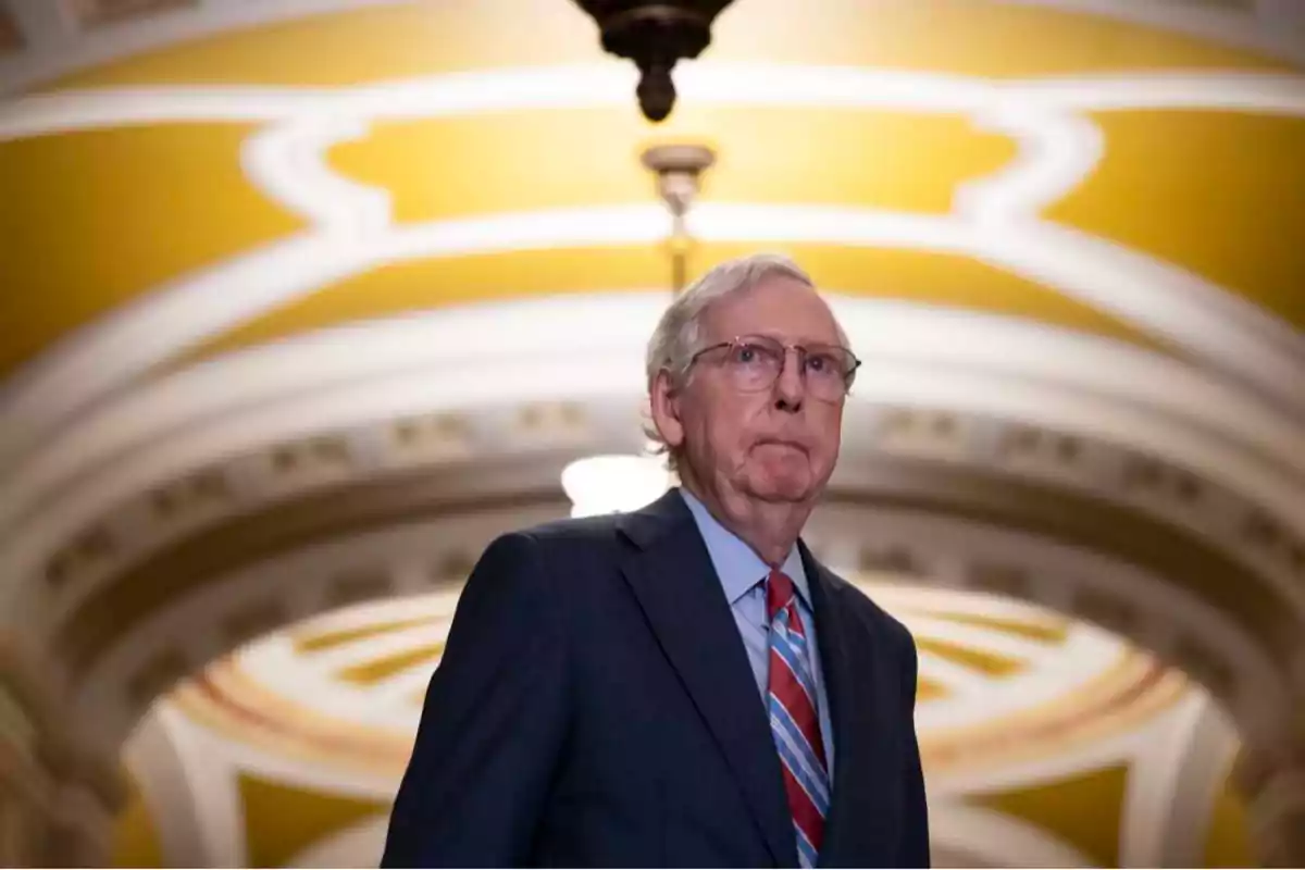 A man in a suit and tie standing under a decorative ceiling in a government building.