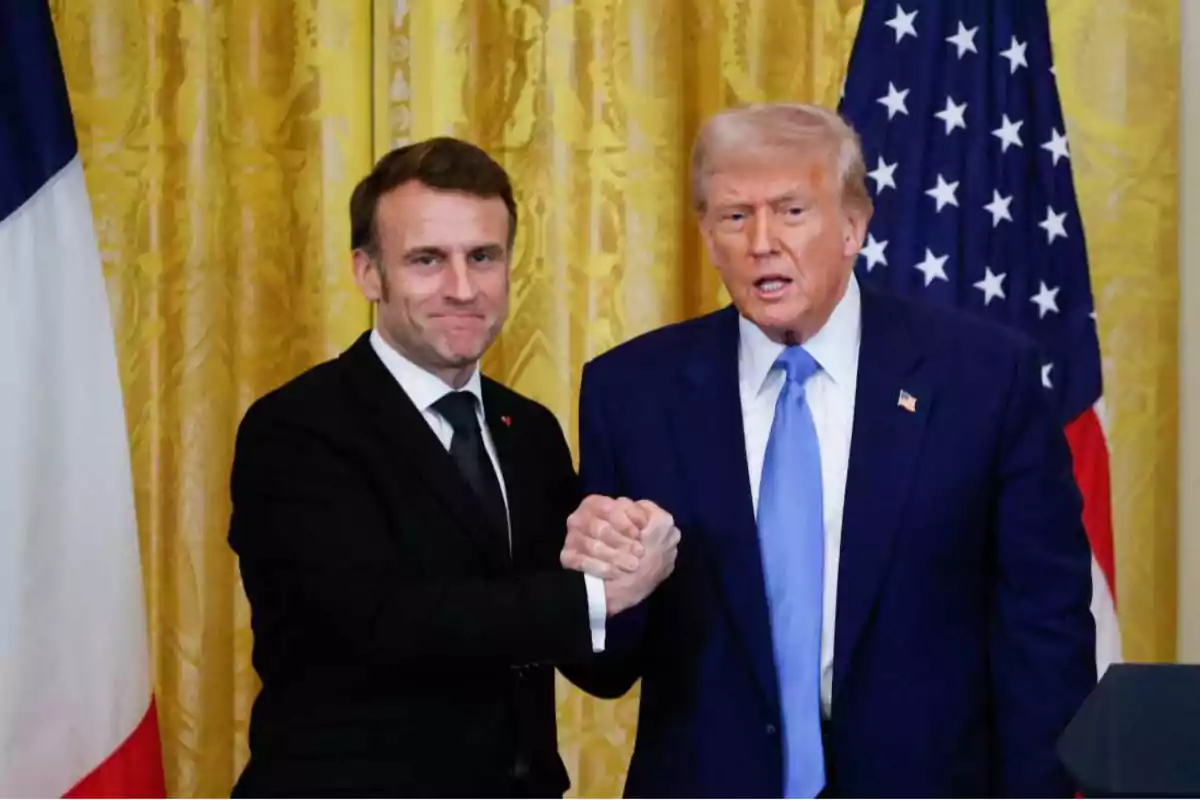 Dos hombres de traje se dan la mano frente a banderas de Francia y Estados Unidos.