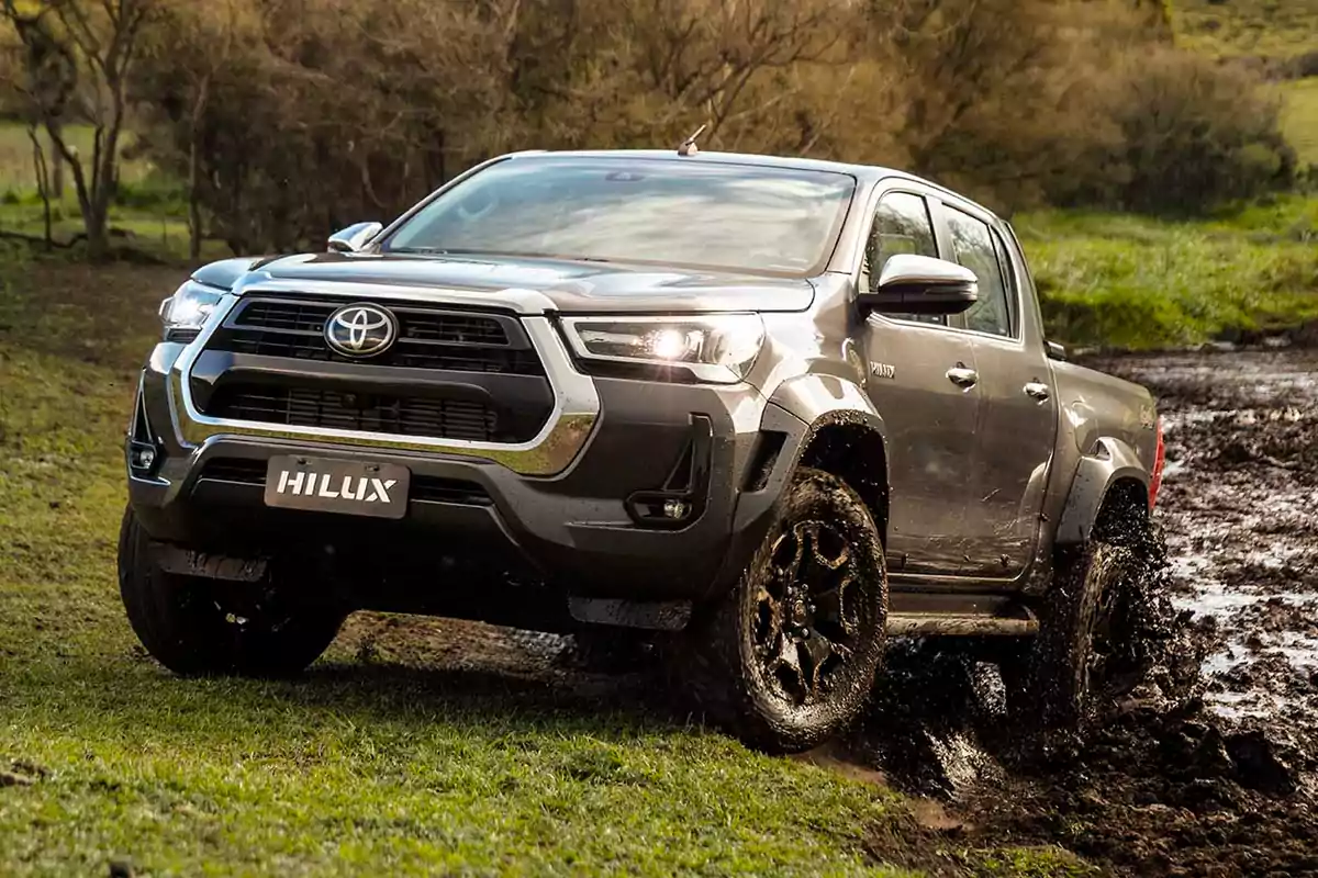 Una camioneta Toyota Hilux de color gris atraviesa un terreno fangoso en un entorno natural.