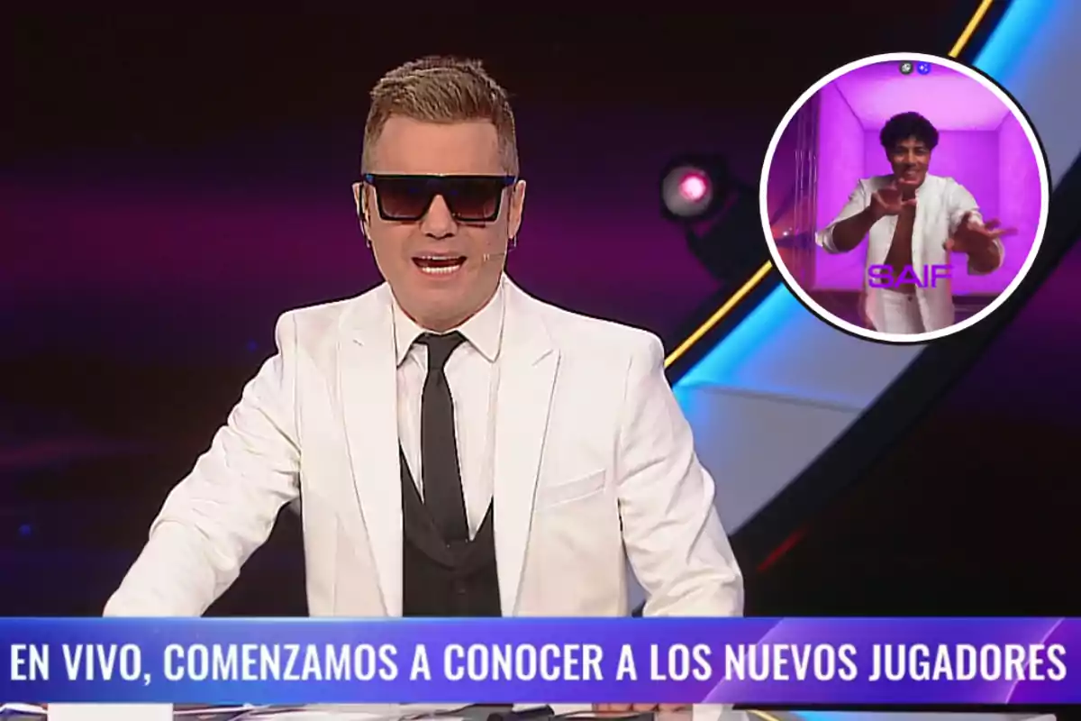 Un presentador de televisión con traje blanco y gafas de sol habla en un programa en vivo mientras en un recuadro aparece un hombre con fondo morado.