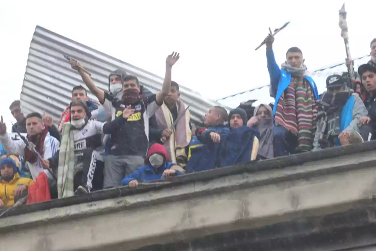 Un grupo de personas se encuentra en un techo, algunas con el rostro cubierto y levantando los brazos.