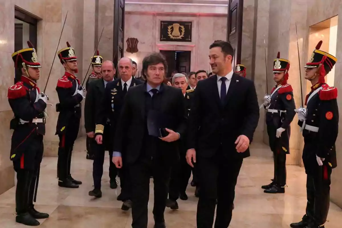 Un grupo de personas camina por un pasillo escoltado por guardias con uniformes ceremoniales y espadas.