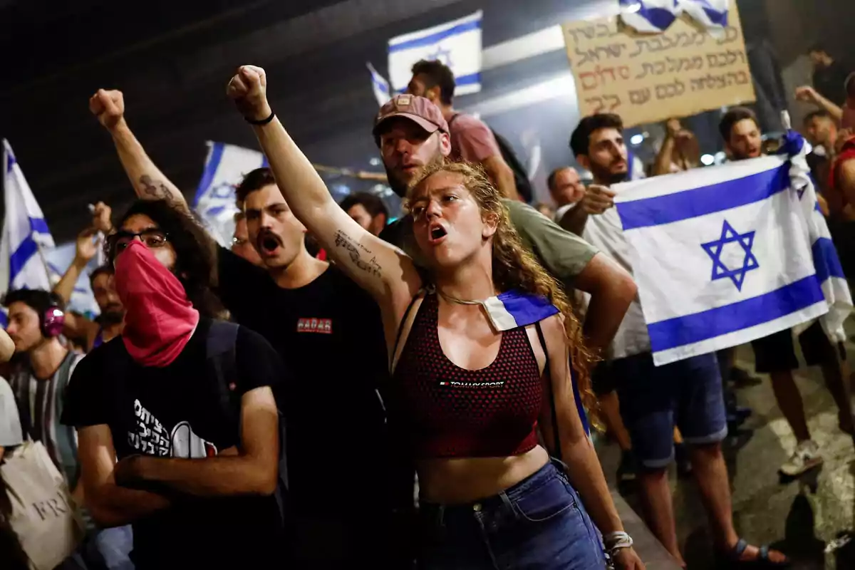 Personas protestando con banderas de Israel y levantando el puño en señal de protesta.